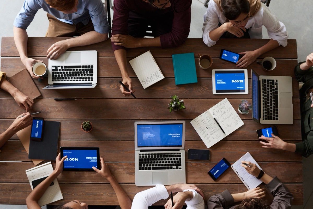 A team's laptops, tablets, and notes spread across a work table during a review