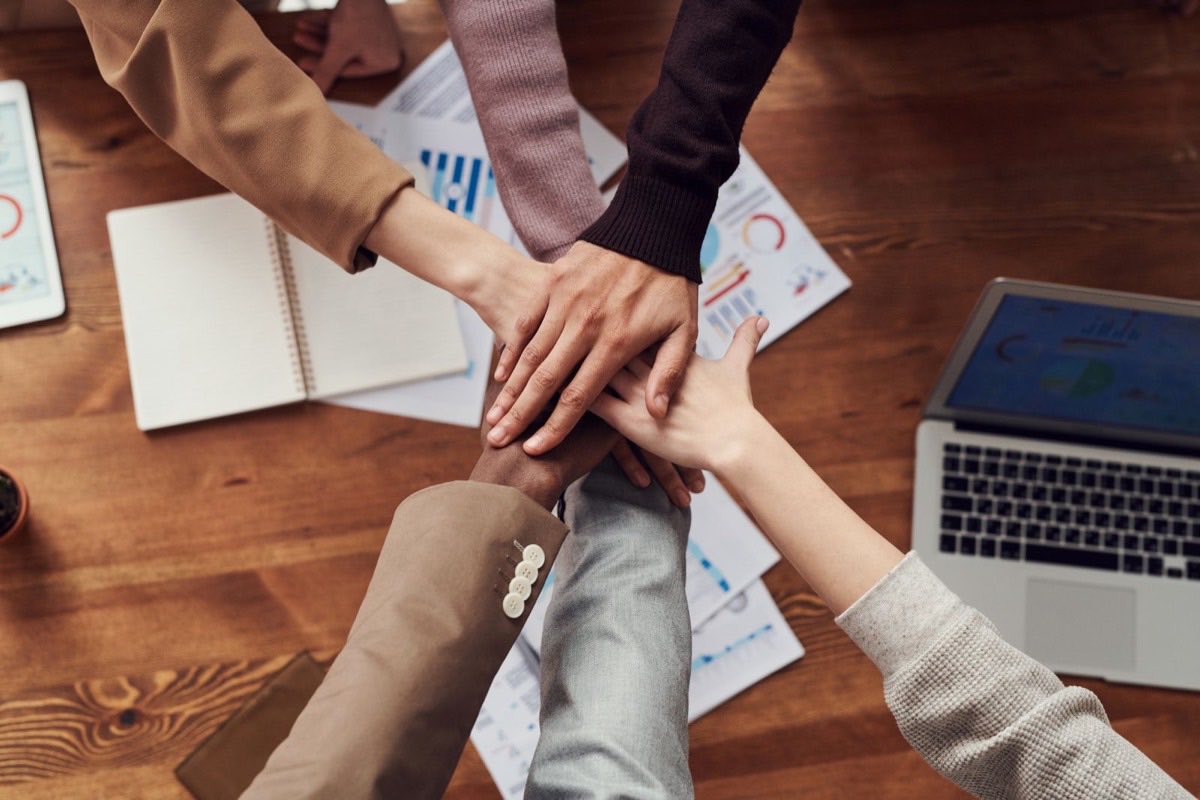 Team members joining hands over a table covered in project plans